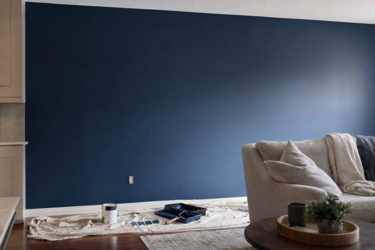 A freshly rolled deep navy accent wall in raking side light, with a paint roller and tray on a drop cloth below