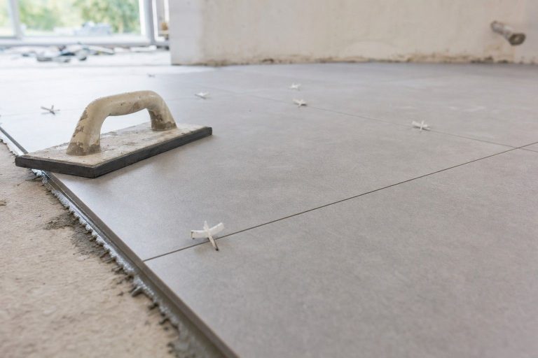 Close-up of a large-format gray tile floor with even grout lines, spacers, and a grout float