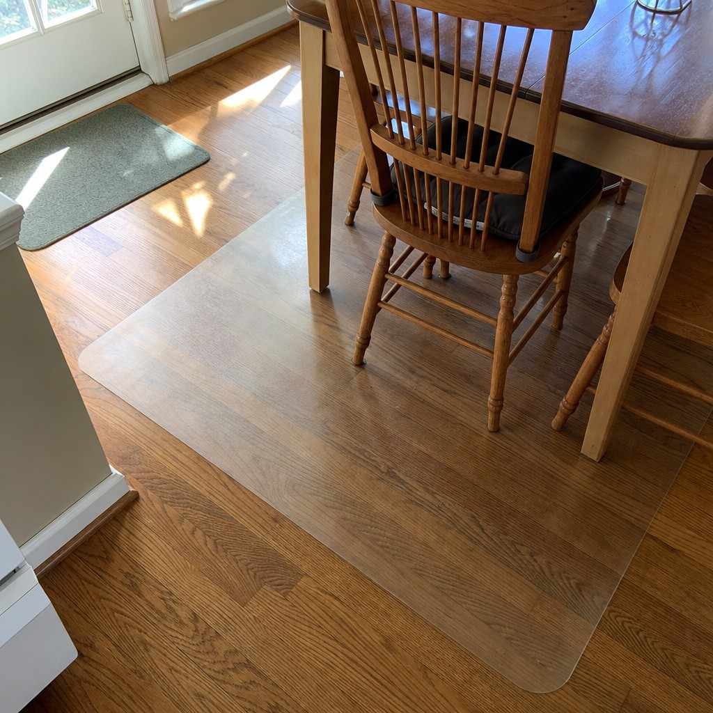 A clear vinyl floor mat protecting hardwood under a kitchen table and chairs